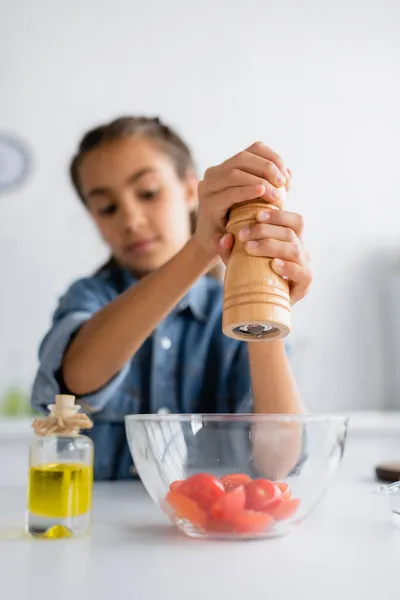 Ragazzo offuscato che condisce pomodori ciliegia in ciotola vicino a olio d'oliva in cucina — Foto stock