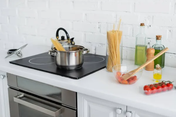 Macaroni near cherry tomatoes and saucepan on stove in kitchen — Stock Photo