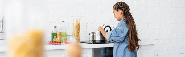 Bambino cucina vicino pentola sui fornelli e ingredienti in cucina, banner — Foto stock