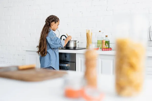 Дитина стоїть біля каструлі і плити під час приготування їжі на кухні — стокове фото