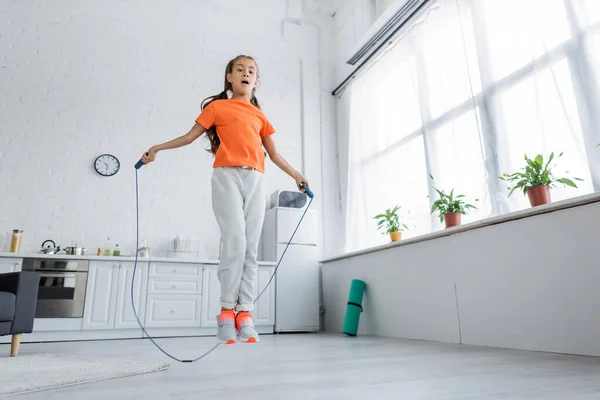 Low angle view of kid jumping with skipping rope in kitchen — Stock Photo