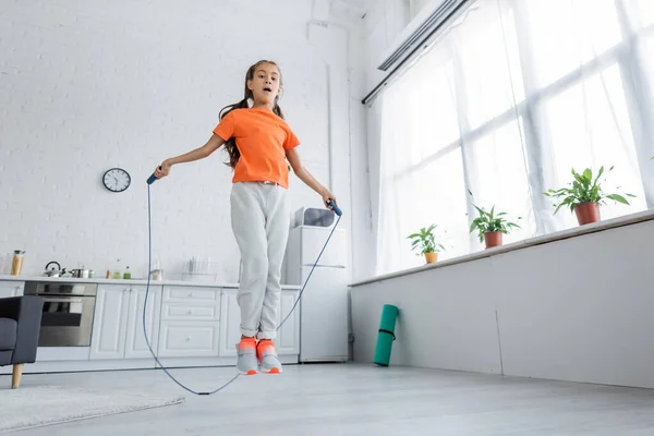 Vue à angle bas du saut d'enfant avec corde à sauter dans la cuisine — Photo de stock