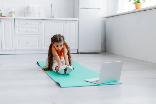 Treinamento infantil em esteira de fitness perto de laptop na cozinha — Fotografia de Stock