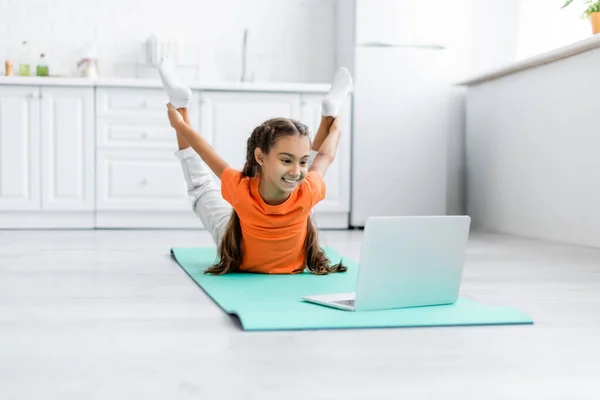 Treinamento menina sorridente perto de laptop no tapete de fitness em casa — Fotografia de Stock