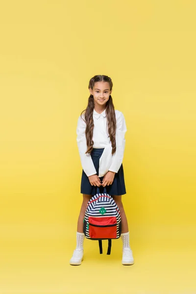 Volle Länge des lächelnden Schulkindes mit Rucksack, das in die Kamera auf gelbem Hintergrund blickt — Stockfoto