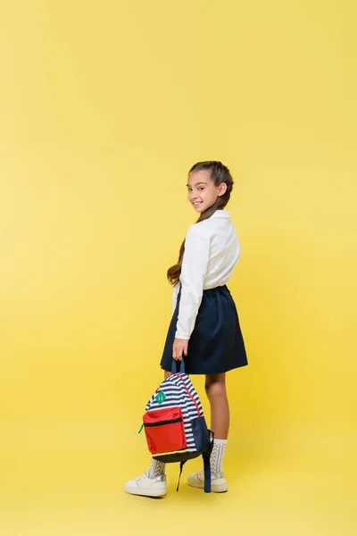 Lächelnder Frühchen-Schüler mit Rucksack blickt in Kamera auf gelbem Hintergrund — Stockfoto