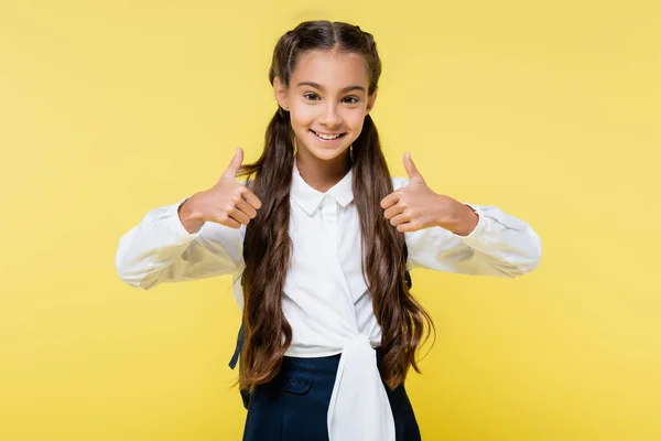 Smiling schoolchild showing thumbs up isolated on yellow — Stock Photo