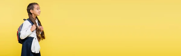 Bambino in età scolare che tiene lo zaino e distoglie lo sguardo isolato su giallo, banner — Foto stock