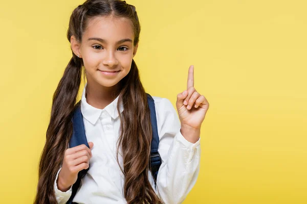 Smiling pupil with backpack having idea isolated on yellow — Stock Photo