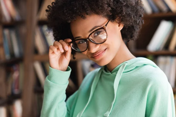 Feliz africano americano estudiante ajustando gafas y mirando a la cámara - foto de stock
