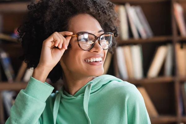 Estudiante afroamericano satisfecho ajustando anteojos y mirando hacia otro lado - foto de stock