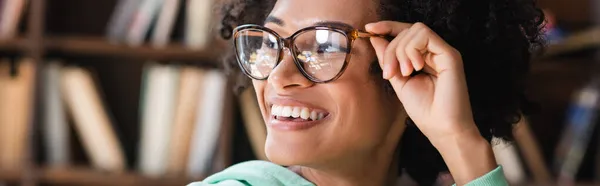 Estudiante afroamericano satisfecho ajustando anteojos y mirando hacia otro lado, bandera — Stock Photo