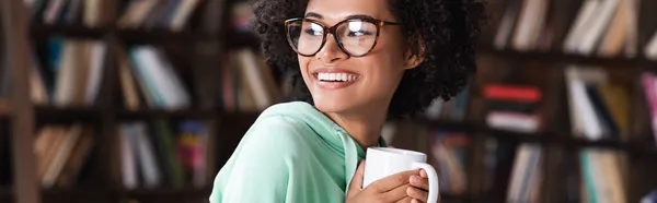 Feliz joven afroamericana mujer en gafas con taza de café, pancarta — Stock Photo