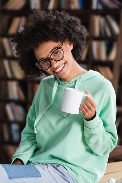 Joyful african american woman in eyeglasses holding cup of coffee — Stock Photo