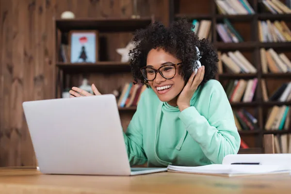 Estudiante afroamericano feliz en gafas y auriculares usando el ordenador portátil - foto de stock