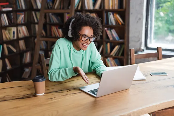 Heureux afro-américain étudiant en lunettes et écouteurs à l'aide d'un ordinateur portable pendant l'appel vidéo — Photo de stock