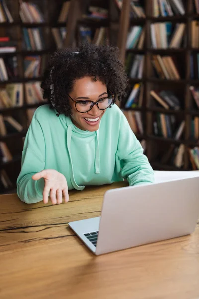 Fröhliche afrikanisch-amerikanische Studentin mit Brille und Kopfhörer per Laptop während eines Videogesprächs — Stockfoto
