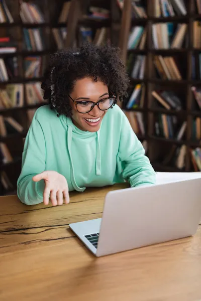 Allegro studente afroamericano in occhiali e cuffie utilizzando il computer portatile durante la videochiamata — Foto stock