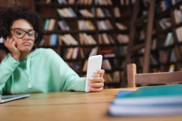 Blurred african american student in eyeglasses using smartphone — Stock Photo