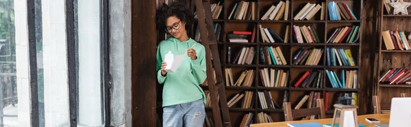 Jeune femme afro-américaine dans des lunettes tenant des baguettes près de la boîte en carton avec de la nourriture à emporter, bannière — Photo de stock