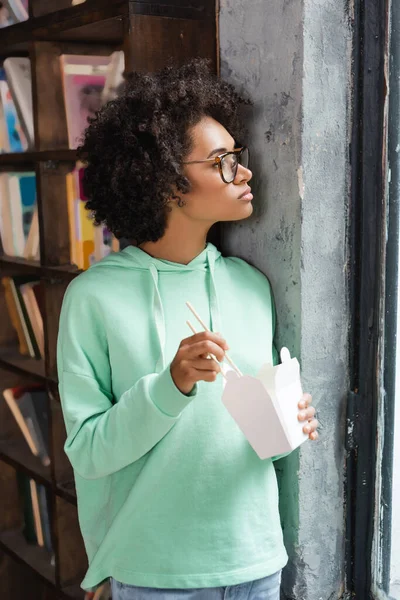 Junge afrikanisch-amerikanische Frau in Brille mit Essstäbchen in der Nähe von Karton mit Imbiss — Stockfoto