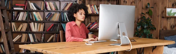 Jovem afro-americana digitando no teclado do computador enquanto olha para o monitor em casa, banner — Fotografia de Stock
