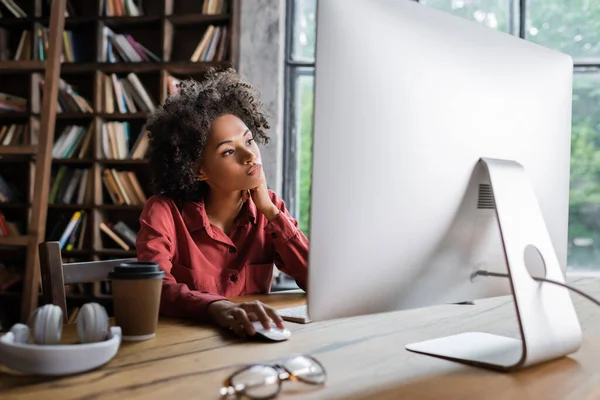 Lockige Afroamerikanerin benutzt Computermaus, während sie zu Hause auf den Bildschirm schaut — Stockfoto