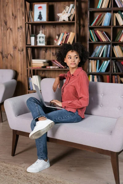 African american woman sitting on couch with laptop — Stock Photo