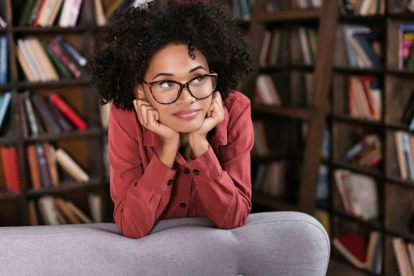 Verträumte afrikanisch-amerikanische Frau mit Brille lehnt auf Couch und schaut weg — Stockfoto