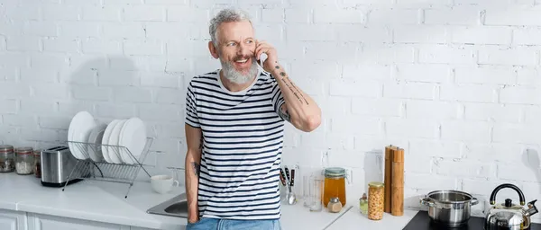 Lächelnder Mann im Smartphone-Gespräch in der Küche, Banner. Übersetzung: 