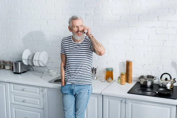 Homem falando no smartphone perto fogão na cozinha. Tradução: 