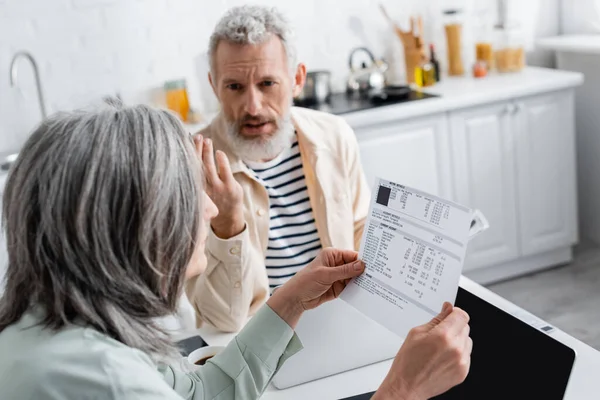 Woman holding bills while husband talking near laptop in kitchen — Stock Photo