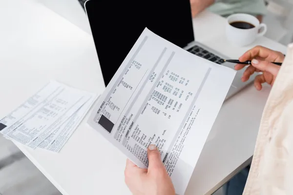 Cropped view of man holding bills near laptop and blurred coffee at home — Stock Photo
