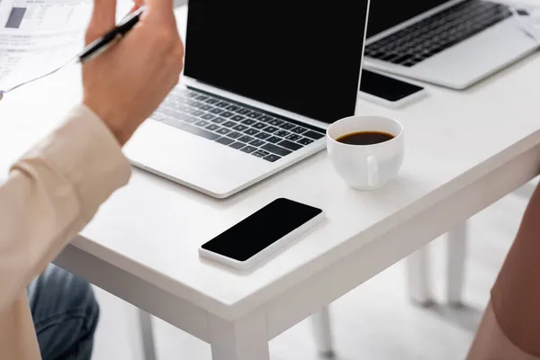 Vista recortada de teléfono inteligente y café cerca del hombre con facturas en casa - foto de stock