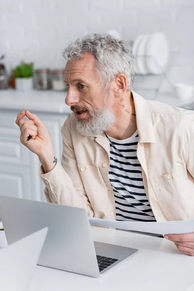 Mature man holding documents near laptops at home — Stock Photo