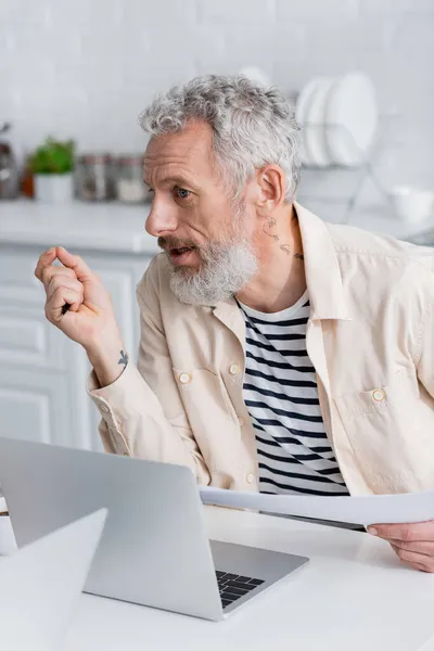 Reifer Mann hält Dokumente in der Nähe von Laptops zu Hause — Stockfoto