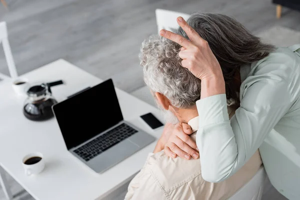 Reife Frau zeigt Friedensgeste in der Nähe ihres Mannes und verschwommene Geräte zu Hause — Stockfoto