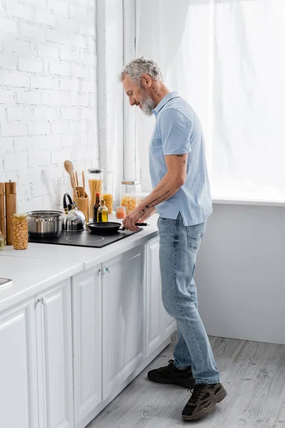 Вид сбоку на человека, готового на плите рядом с едой на кухне — стоковое фото