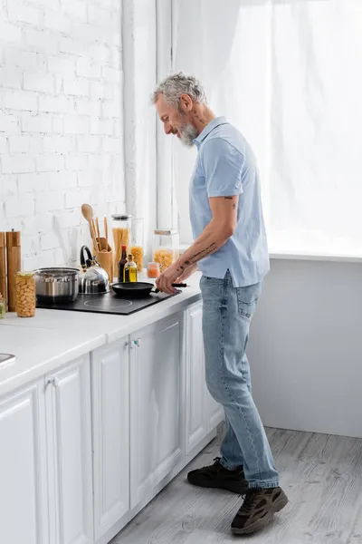 Seitenansicht eines Mannes, der auf Herd in der Nähe von Lebensmitteln auf Küchenarbeitsplatte kocht — Stockfoto