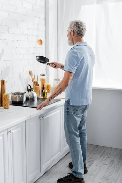 Homem tatuado a cozinhar panqueca na cozinha. Tradução: 