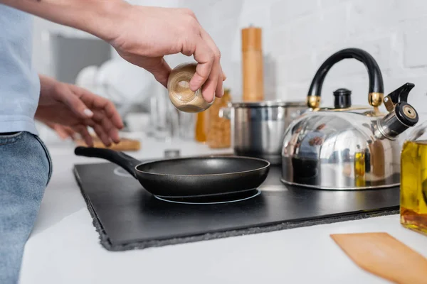 Vista ritagliata dell'uomo che tiene la spezia vicino alla padella sui fornelli in cucina — Foto stock