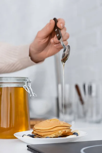 Vue recadrée de la femme versant du miel sur des crêpes avec des baies dans la cuisine — Photo de stock