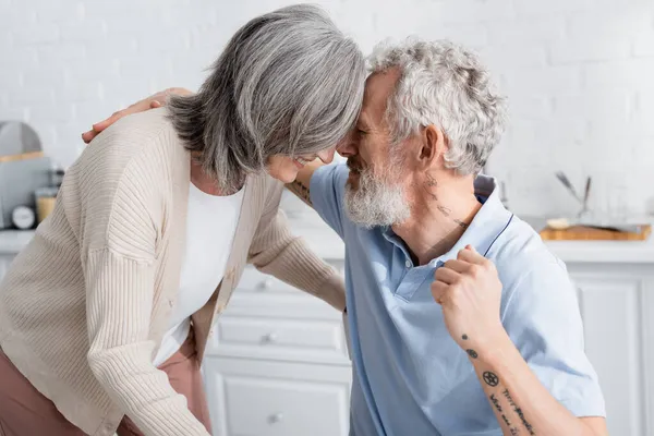 Maturo uomo abbraccio sorridente moglie in cucina — Foto stock