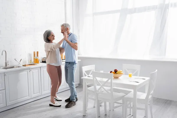 Усміхнена пара середнього віку танцює на кухні — стокове фото