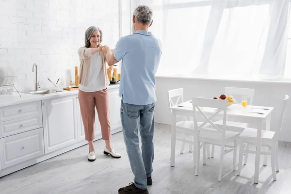 Mulher positiva segurando a mão do marido maduro na cozinha — Fotografia de Stock