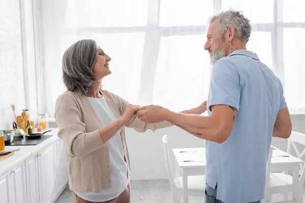 Seitenansicht eines lächelnden Paares mittleren Alters, das in der Küche tanzt — Stockfoto