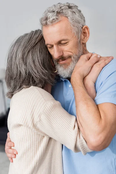 Woman embracing mature husband with closed eyes at home — Stock Photo