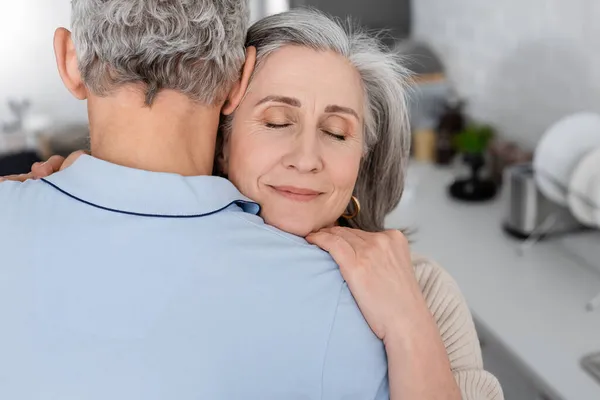 Mujer de mediana edad abrazando marido en la cocina - foto de stock