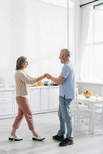 Seitenansicht eines Paares mittleren Alters, das neben Früchten und Orangensaft auf einem Tisch tanzt — Stockfoto