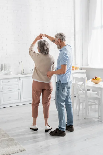 Couple d'âge mûr dansant près des fruits sur la table dans la cuisine — Photo de stock